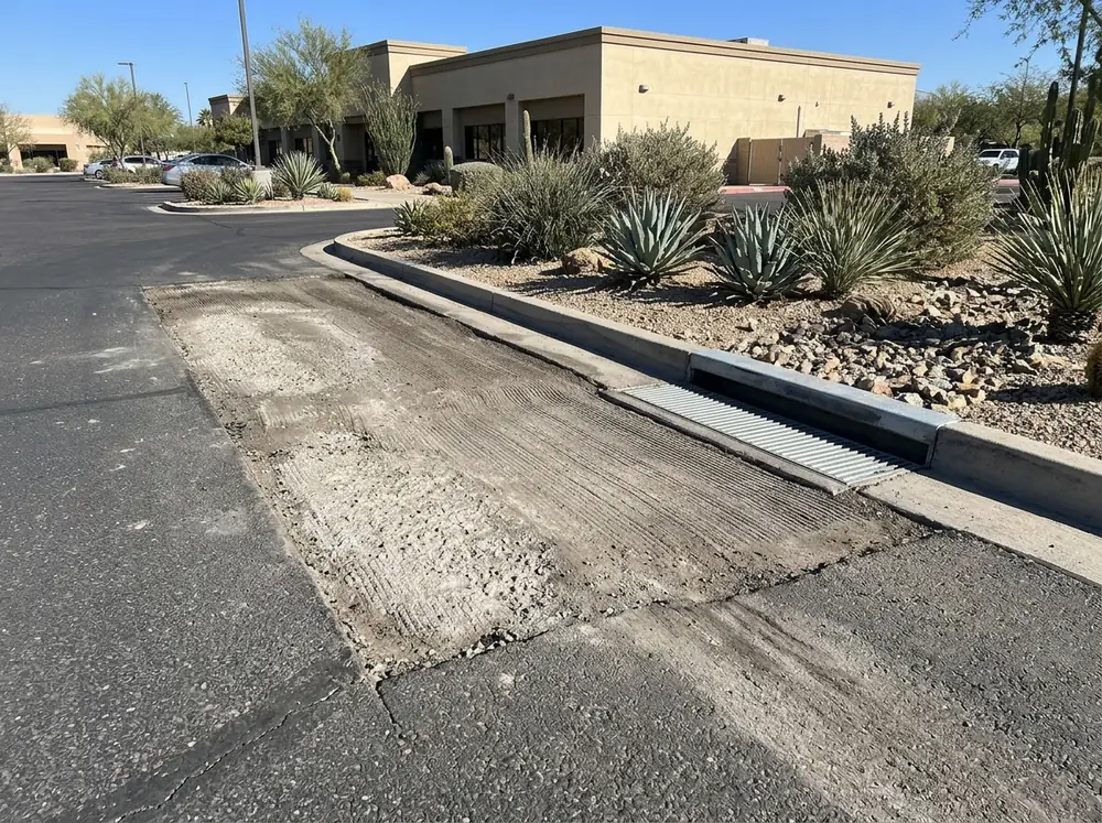 Shallow milled area along a drive lane in a parking lot where water used to pond, the grooves sloping toward a drain