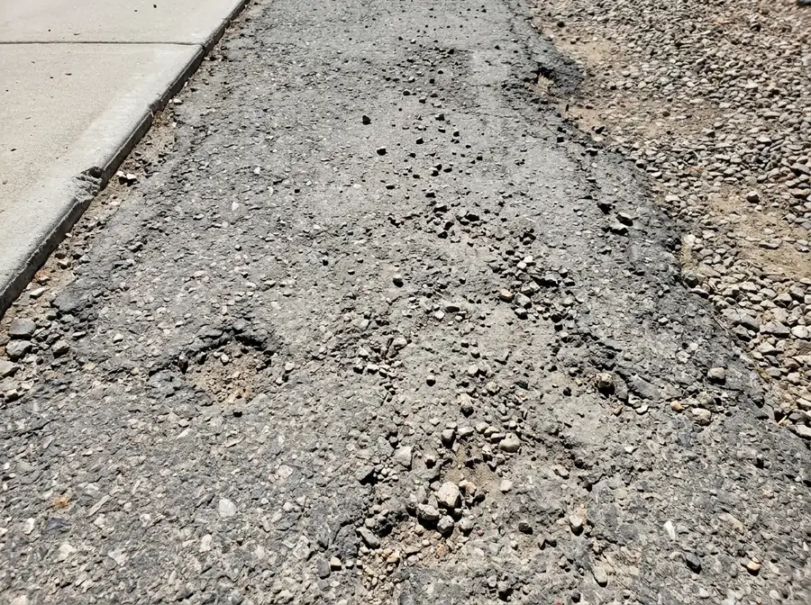 Raveled gray asphalt driveway surface with loose stones and exposed aggregate