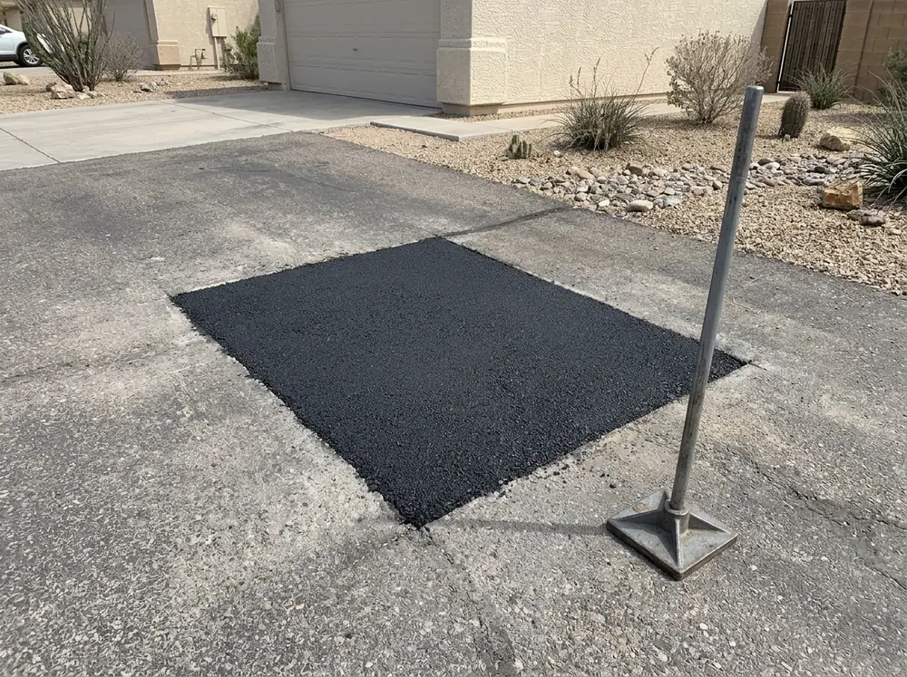 Saw-cut rectangular patch of fresh asphalt in an older driveway, prepared before a full overlay