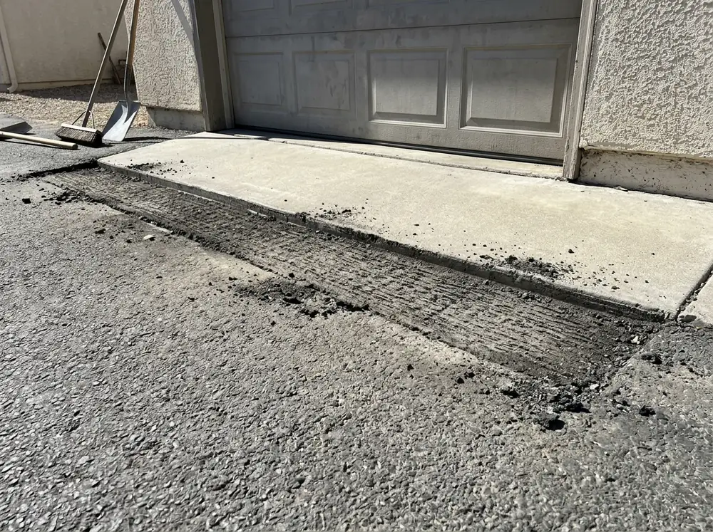 Milled strip along the garage slab of an asphalt driveway, ready for a new overlay to meet the concrete flush
