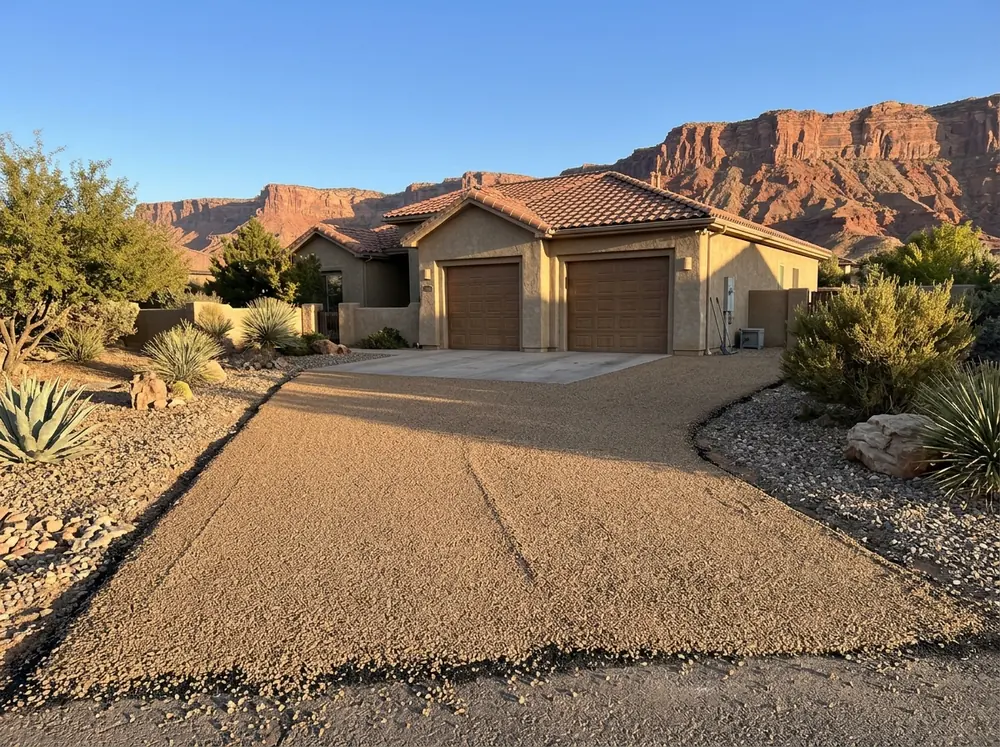 Freshly chip-sealed driveway with a uniform layer of tan crushed stone leading to a stucco home's garage