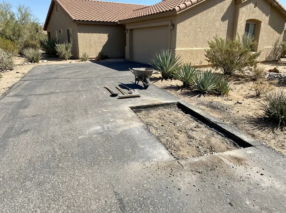 Rectangular saw-cut section of a driveway removed down to the gravel base while the rest of the asphalt stays in place