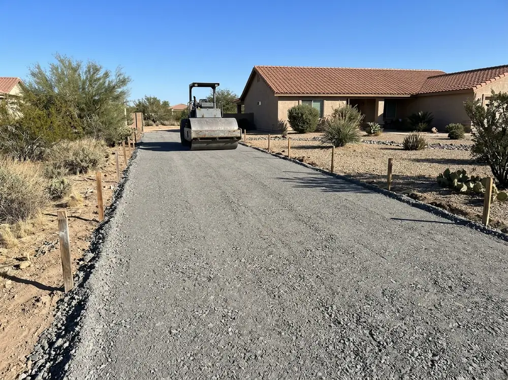 Layer of gray crushed road base spread and rolled flat over a prepared driveway bed, edges staked